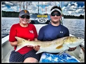 man and woman holding big redfish