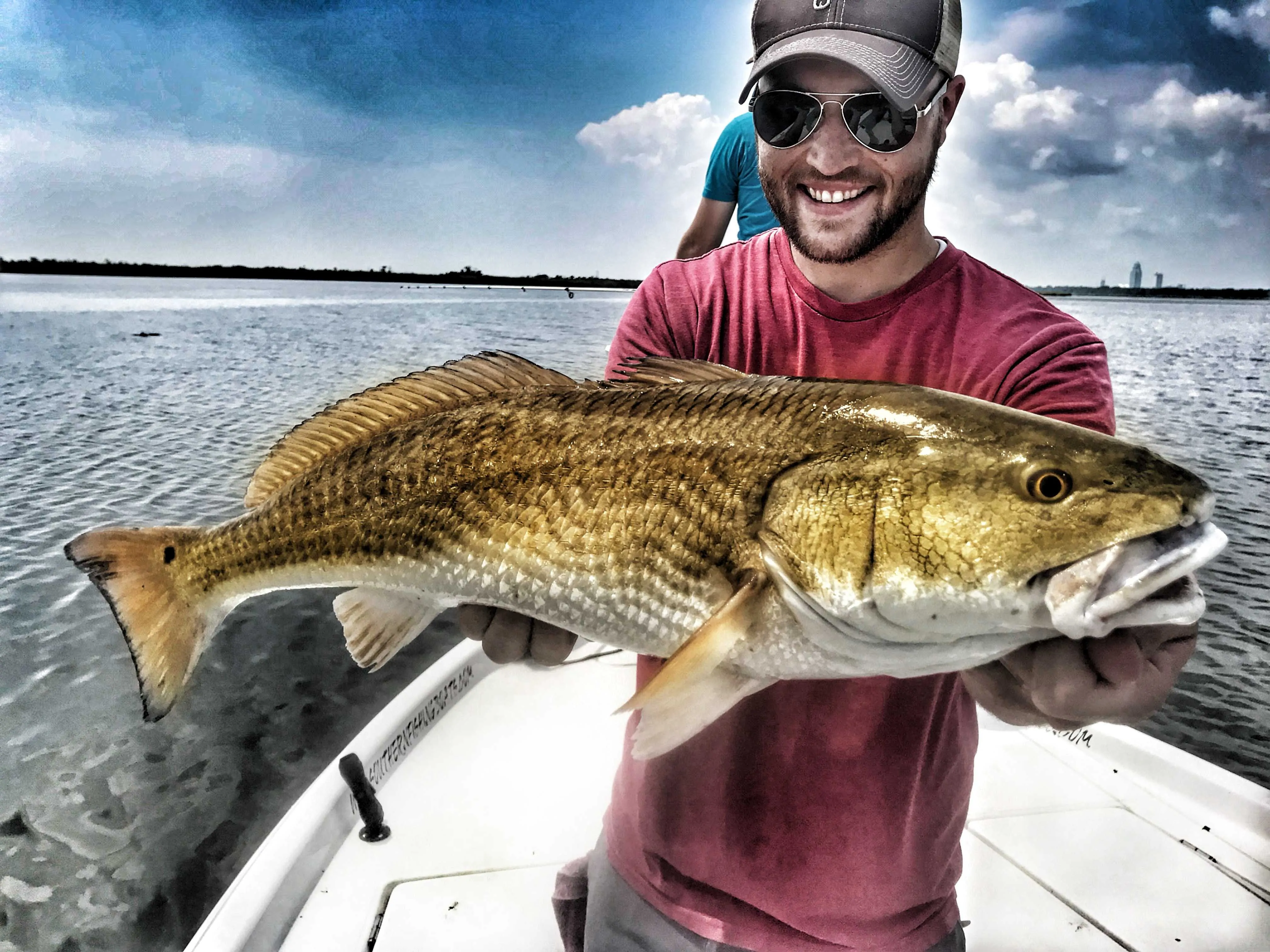 man-smiling-holding-big-redfish-while-standing-in-boat