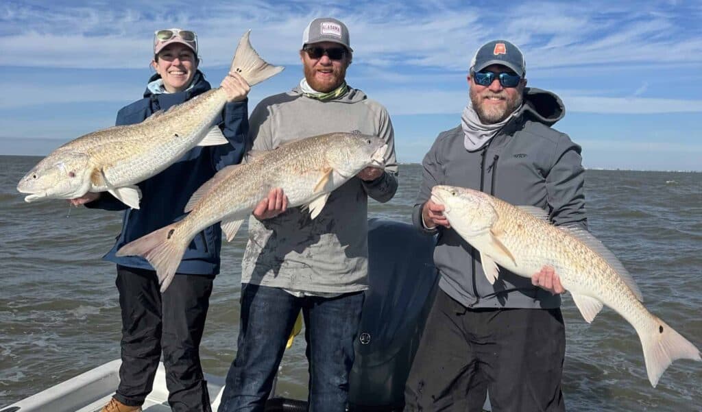 Three anglers with large redfish catches.